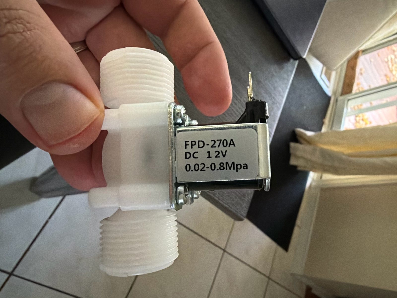 The FPD-270A solenoid valve: white plastic body, threaded both ends, a metal coil frame labelled DC 12V 0.02-0.8MPa