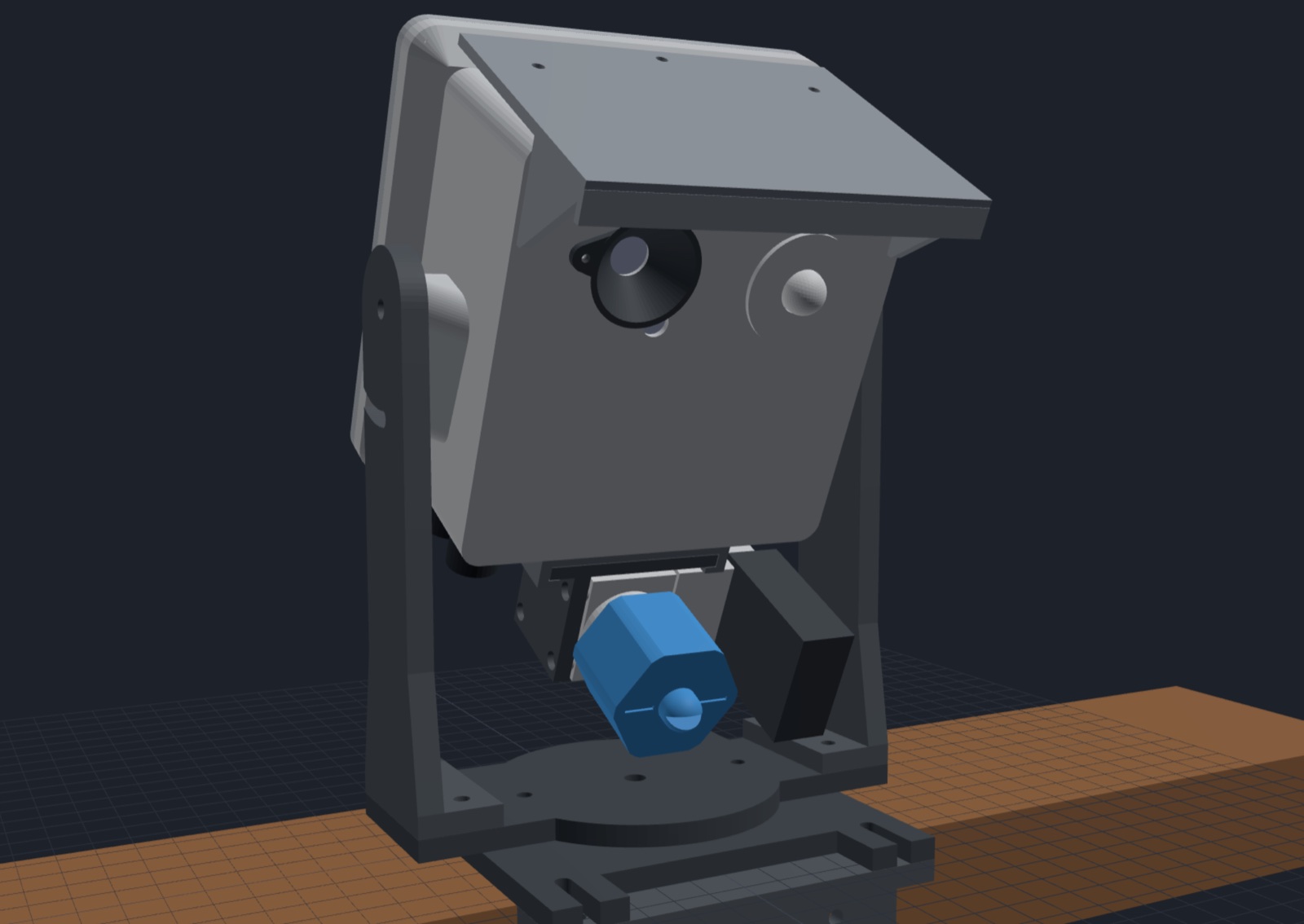 The same enclosure assembled, from the front: the grey box with its rain hood and lens hood, the valve and its blue nozzle under it, all on the yoke over a wooden rail