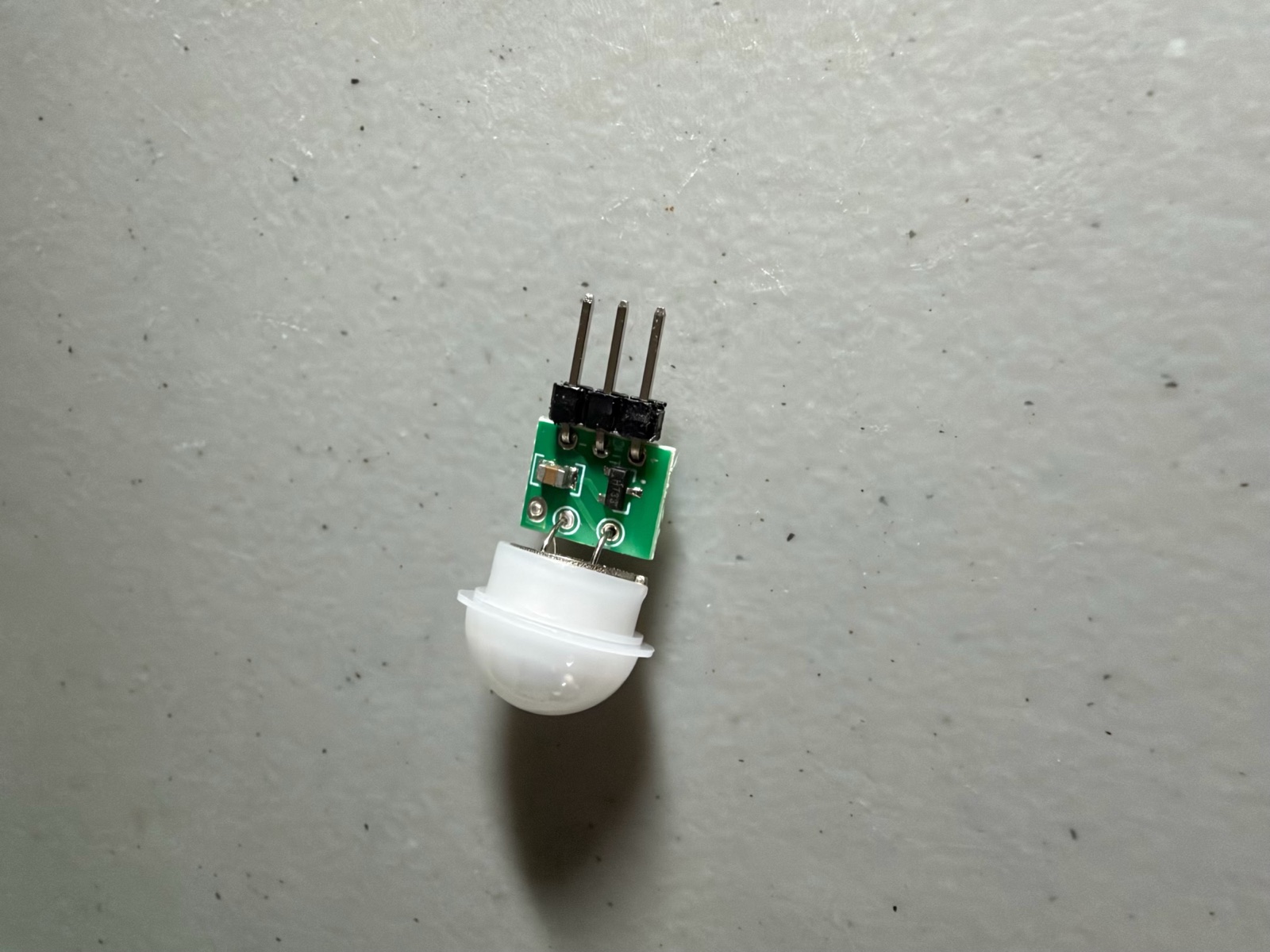 The AM312 mini PIR: a small green board with three pins, and a white dome about 12 mm across