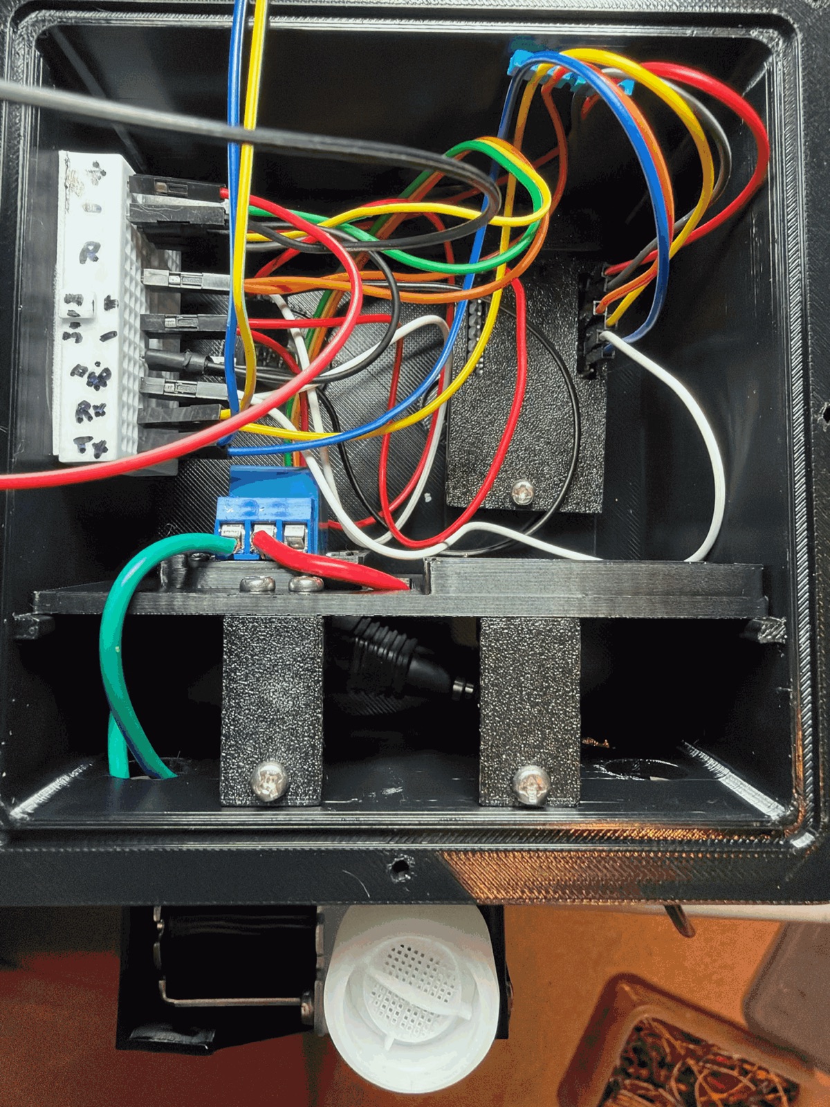 Looking into the box from the back: a 170-pin breadboard glued to the left wall with jumpers to the camera's pins, the sled across the middle with the relay's blue screw terminal, the two sled brackets screwed in below it in the cable basement, and the valve's white inlet under the box