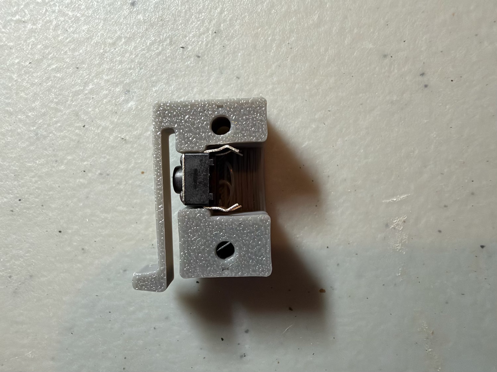 The home switch holder from the side, with the black tactile button sitting loose in its pocket, its legs bent out at the back