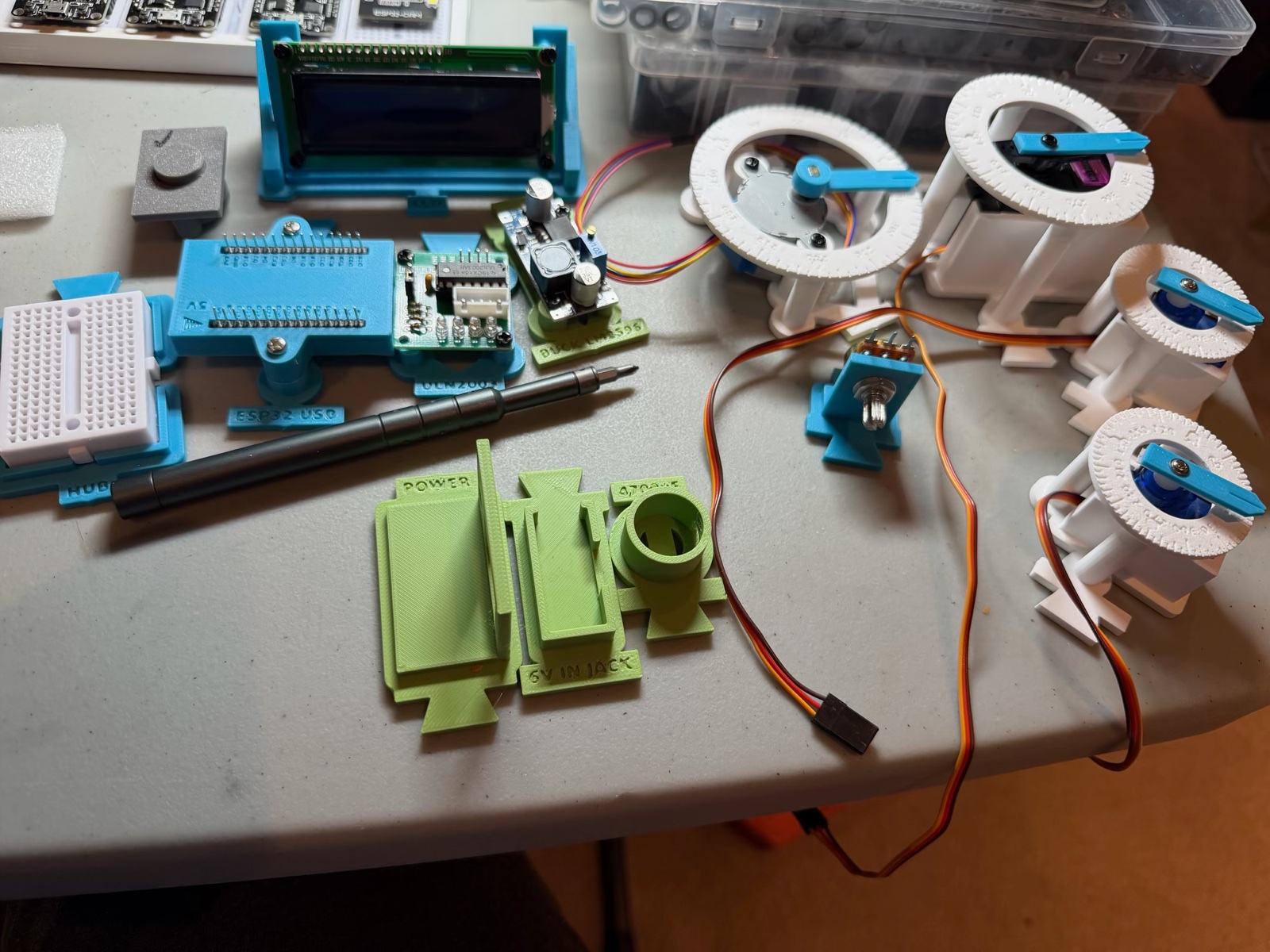 The v2 modules on my desk: the LCD, ESP32 carrier, ULN2003, buck and hub with its mini breadboard on the left, the green power modules in front, and on the right the stepper's dial and three servo dials with their pointers fitted